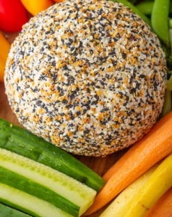 Everything bagel Cheese ball on a platter with carrots, cucumbers, peppers and sugar snap peas