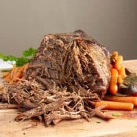 Instant Pot Pot Roast with veggies being sliced on a butcher block