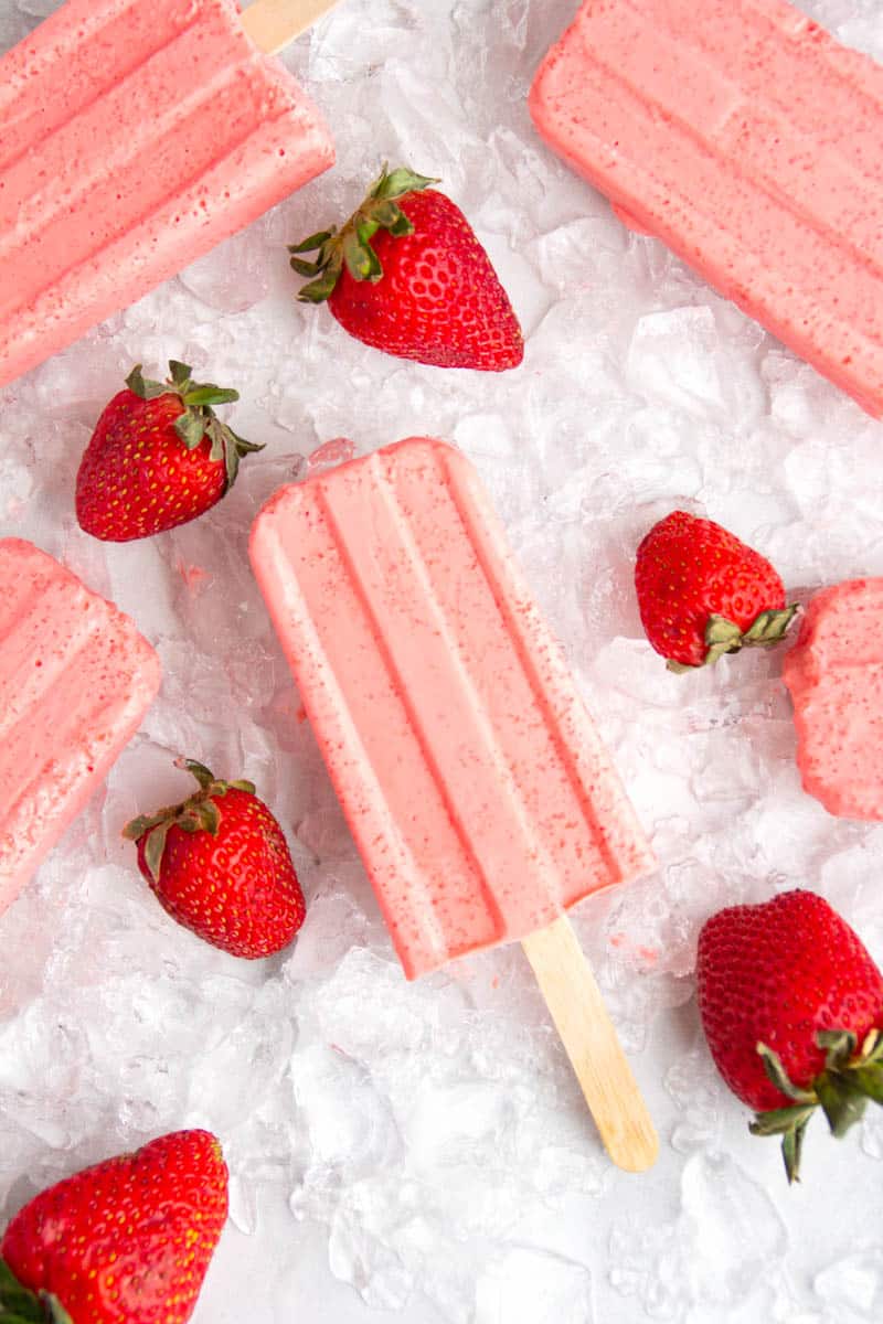 Keto Strawberry Popsicles laying on ice with a few strawberries