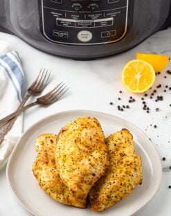 Lemon pepper air fryer chicken on a plate with the air fryer in the background