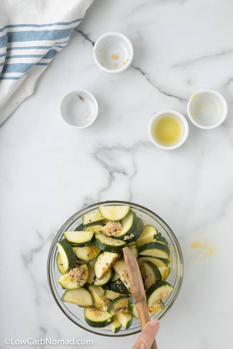 fresh cut zucchini in a glass bowl with seasonings and olive oil